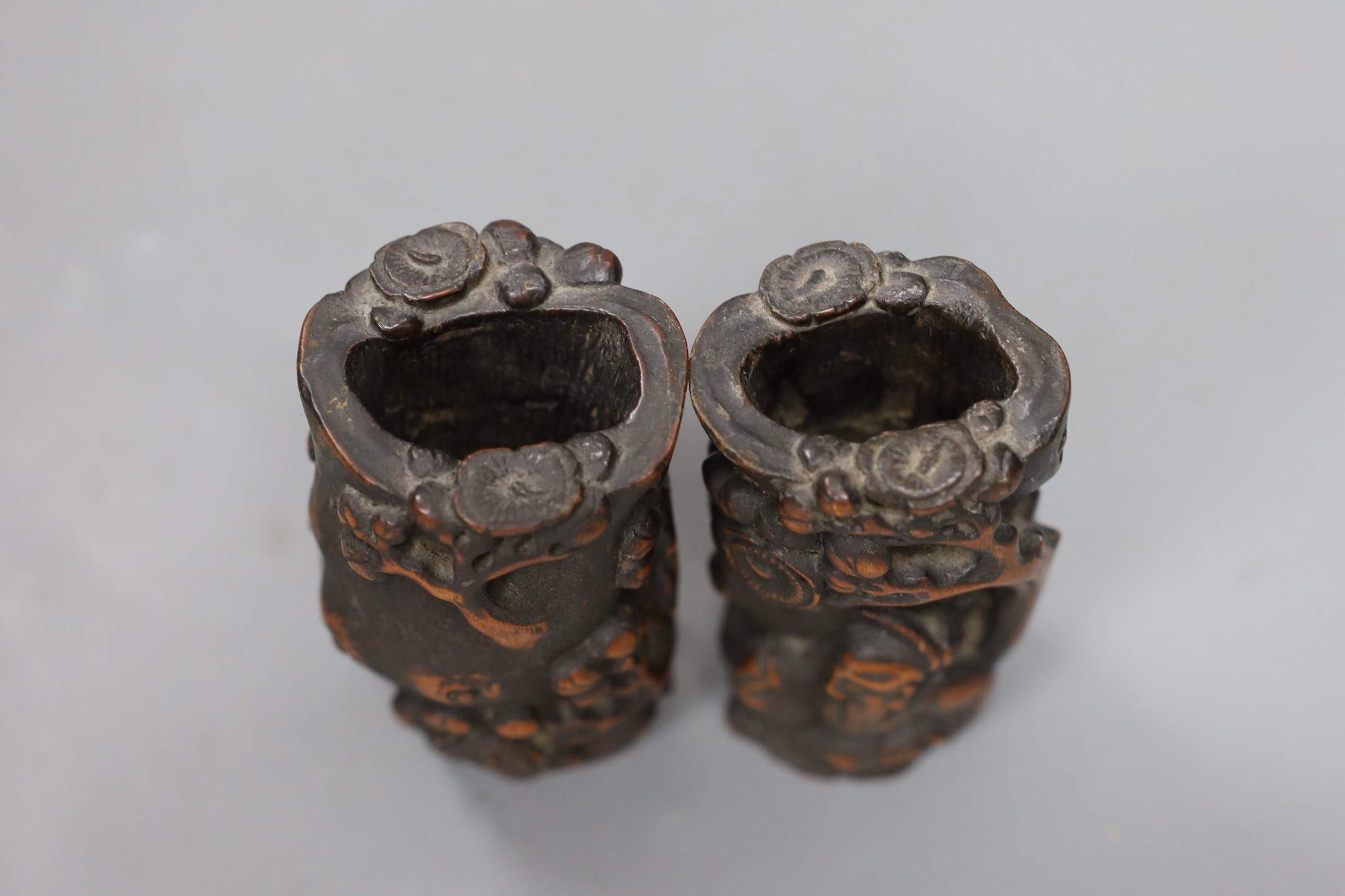 A pair of Chinese carved bamboo brush pots, late Qing dynasty, carved in high relief with a sage beneath a prunus tree, 11cms high